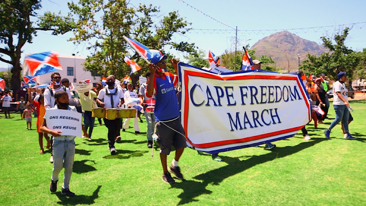 A wide street-level view of demonstrators marching peacefully along an urban avenue in South Africa, with crowds walking in loose formation