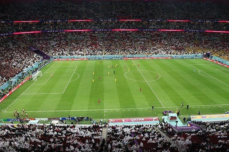 A packed football stadium at night with players gathered near a goal during a knockout match, illuminated by bright floodlights.