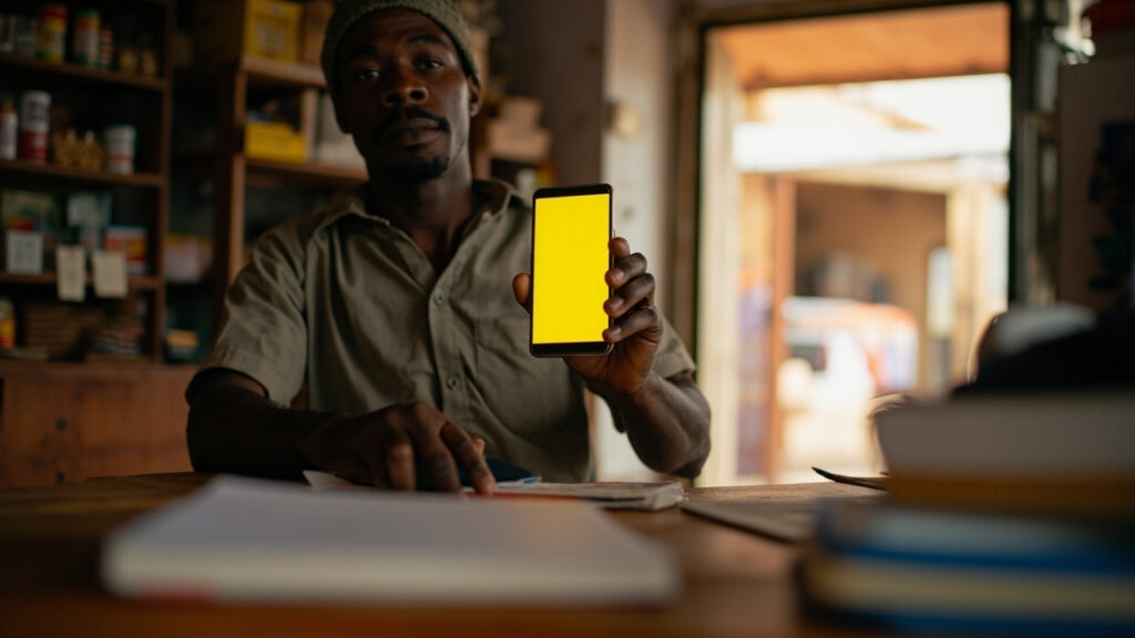 A small shopkeeper in Kenya using a mobile phone to handle a payment at the counter of a retail store.