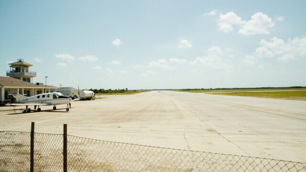 A small regional airport runway and control tower in southeastern Africa under clear daylight skies, with a parked light aircraft on the tar