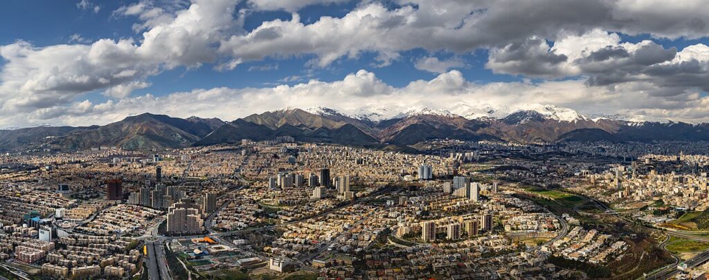 A panoramic daytime view of a sprawling Middle Eastern capital city with concrete administrative buildings and distant hills on the horizon.