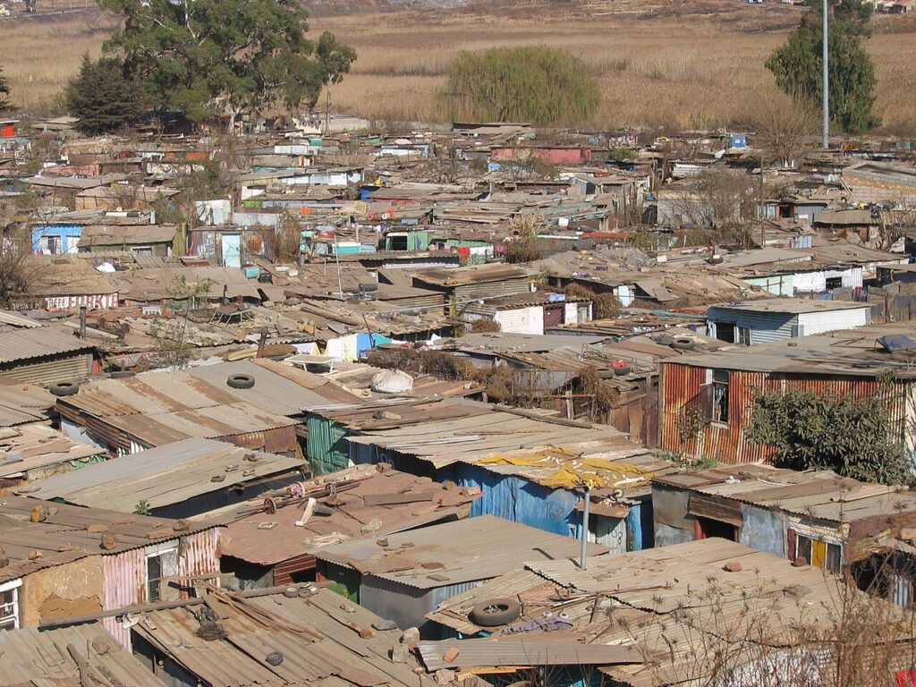 A residential street in a South African township showing rows of small houses, overhead power lines and a communal water tap under a clear s