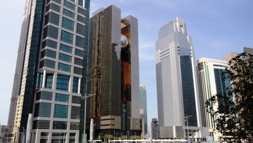 A wide view of a modern Gulf city skyline at dusk, with diplomatic quarter buildings and cranes visible in the foreground.