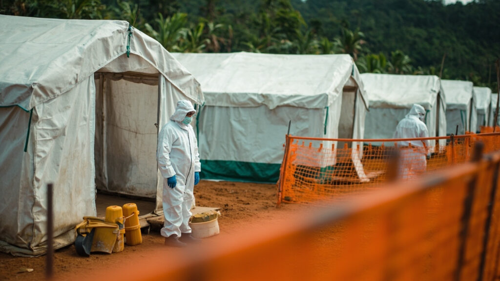 Medical workers wearing protective suits and masks stand outside an Ebola treatment facility with canvas tents and disinfection equipment vi