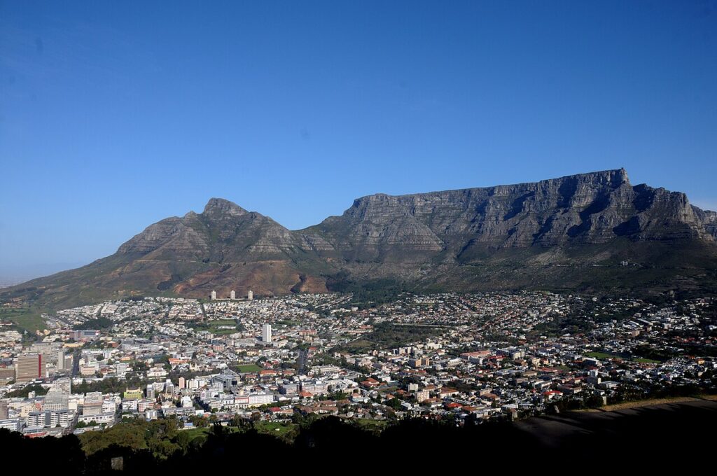 A panoramic view of Cape Town's urban coastline with Table Mountain rising in the background at dusk, harbour waters in the foreground.