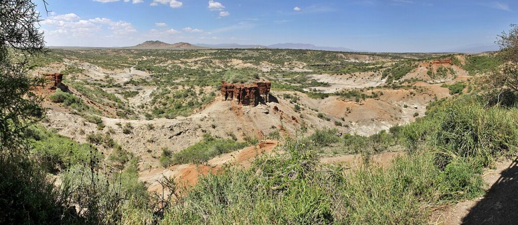 An arid archaeological excavation site with exposed rock strata, hand tools and a small team working on dusty ground.