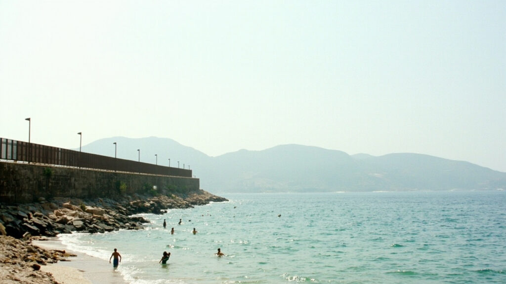 A wide coastal view of the Strait of Gibraltar with a fortified shoreline, calm blue water and distant hills on the horizon under daylight.