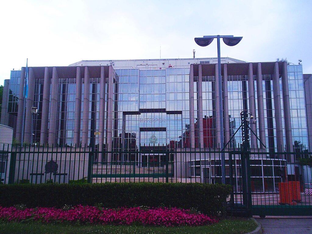 A photograph of an institutional headquarters building with a plaza in the foreground, illustrating an international law enforcement setting