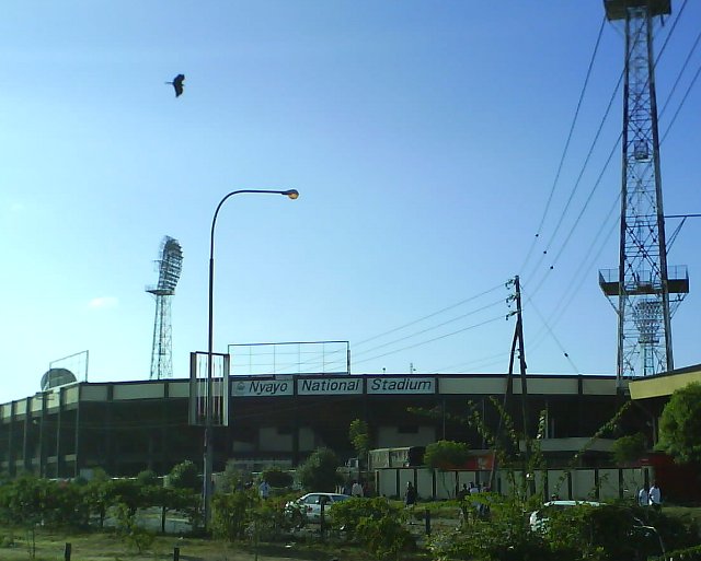 A modern athletics stadium with a running track and seating in an African city at dusk.
