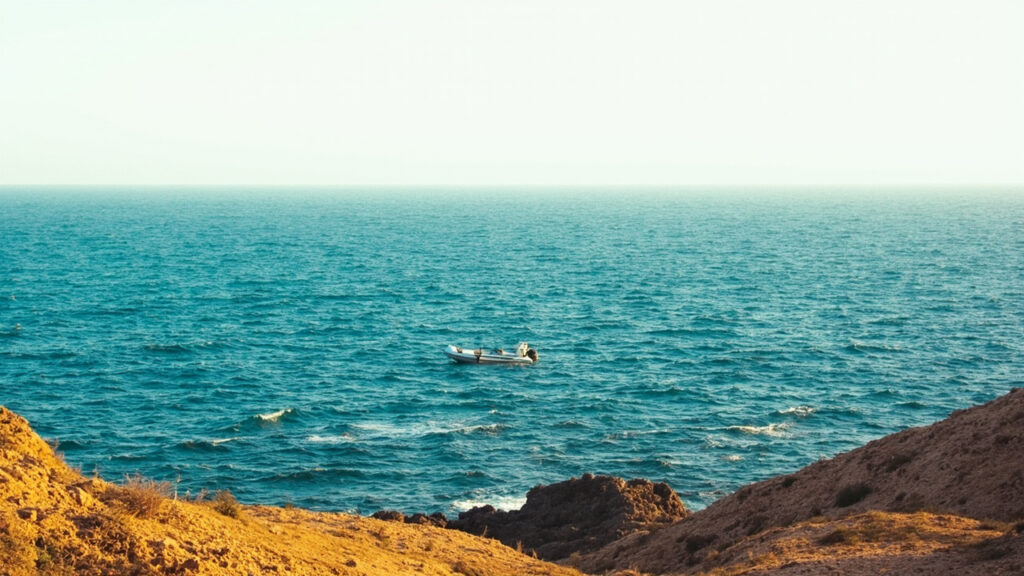 A view of a rocky North African coastline with choppy Mediterranean waters and a small distant vessel at sea.