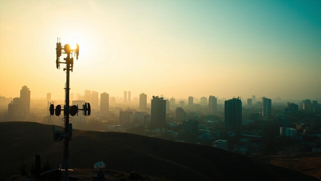 A tall telecommunications mast with antenna arrays rises above a mid-rise urban skyline of glass and concrete office buildings at golden hou