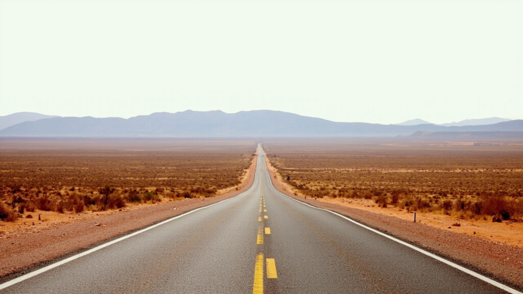 A long straight paved road stretching across an arid Namibian landscape toward distant flat-topped mountains under a clear sky.