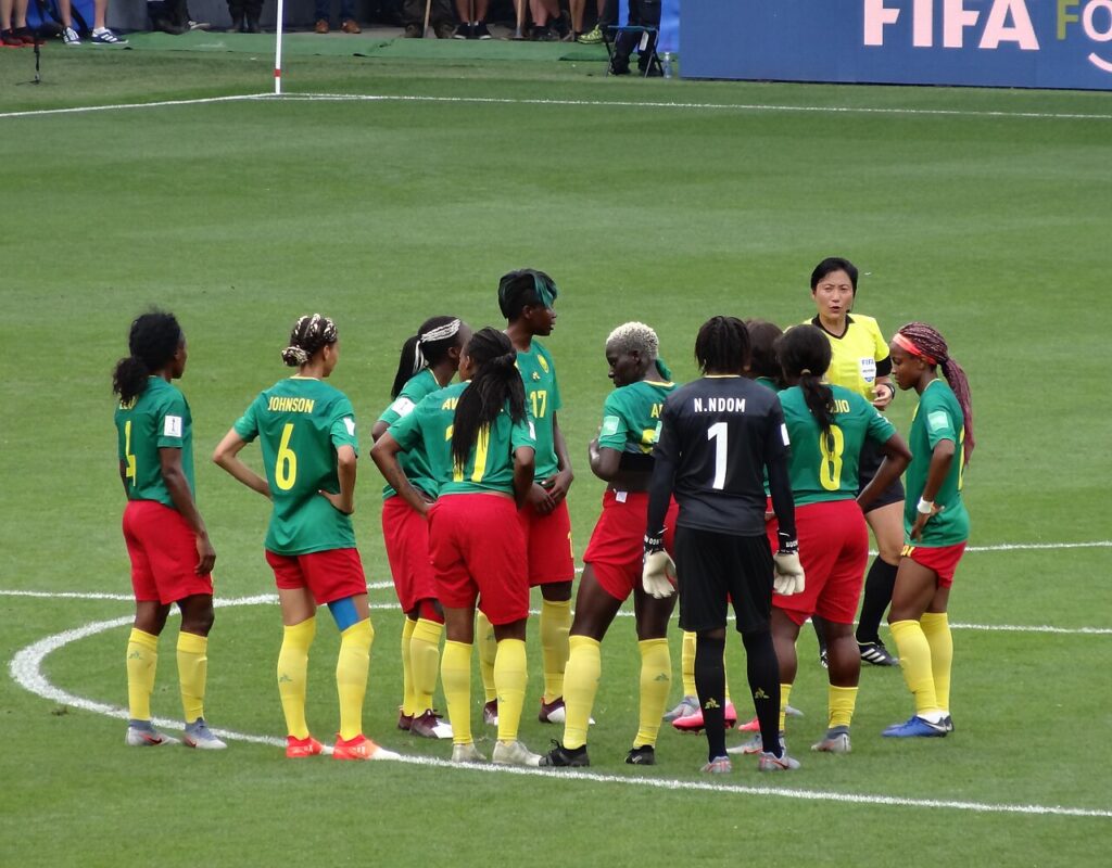 Cameroon women's football players celebrating with a trophy on a stadium pitch after winning a continental final.