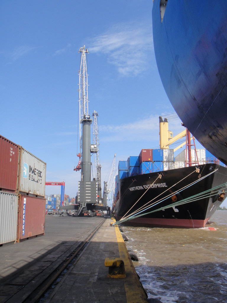 A wide view of the container terminal at Apapa Port in Lagos, with stacked shipping containers, gantry cranes and a docked cargo vessel unde