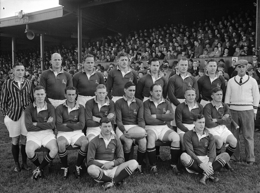A rugby team in green and gold walks onto a stadium field before an international Test, with spectators seated in the stands behind them.