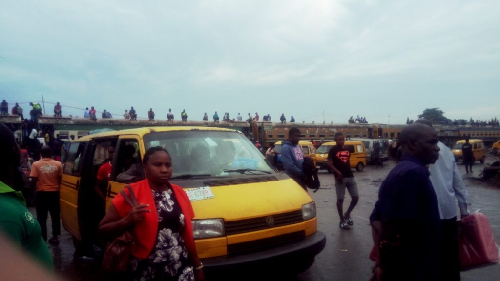A photograph showing a vehicle at an electric charging station with urban infrastructure in the background, illustrating Nigeria's transport