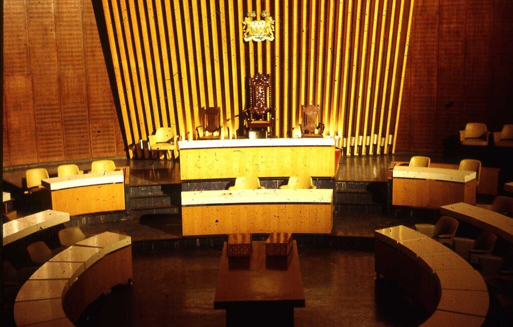 A wide view of the Sierra Leone Parliament building in Freetown, with tropical vegetation and a clear sky in the background.