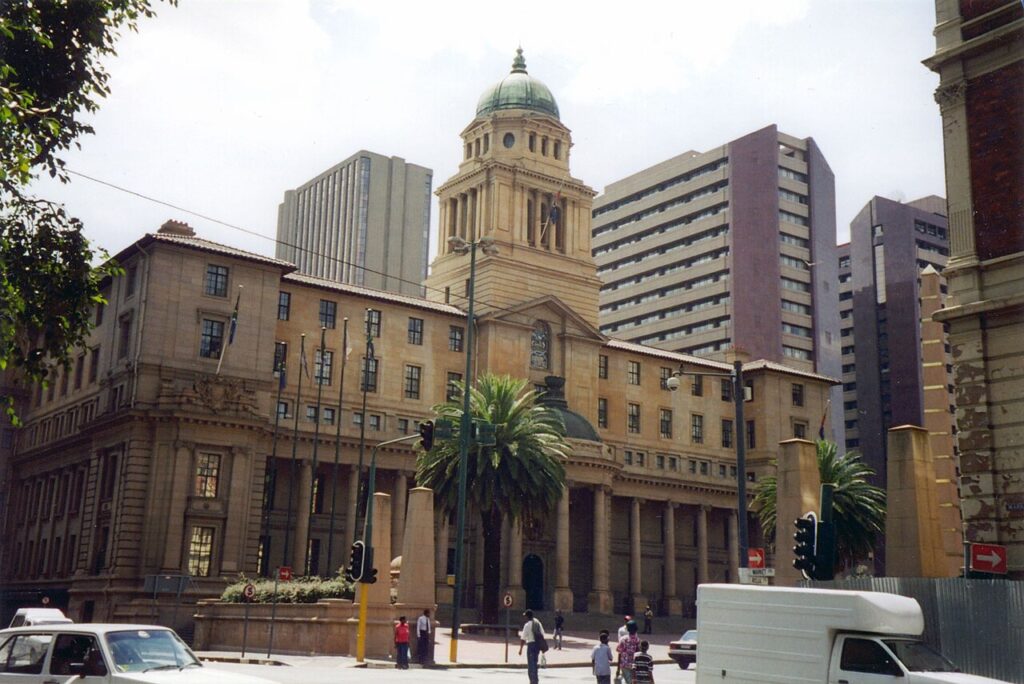 A bustling urban street scene in a major South African city, with commercial buildings, traffic and pedestrians at golden hour.