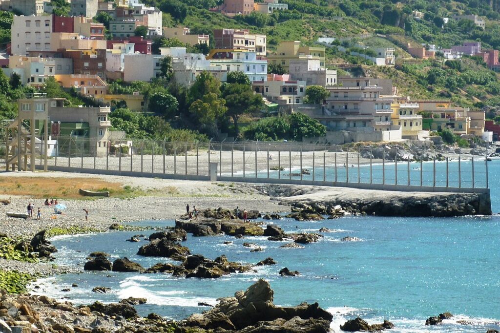 A coastal view of the border area between the Spanish enclave of Ceuta and Morocco, showing the border fence and Mediterranean Sea beyond.
