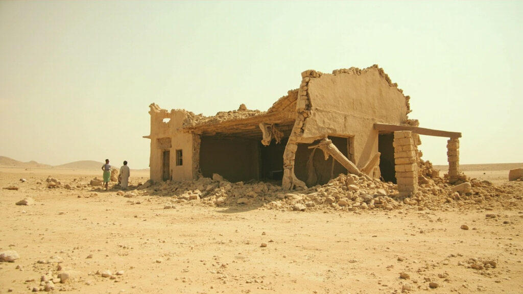 A damaged rural building in an arid North Darfur landscape strewn with debris and dust after an airstrike.