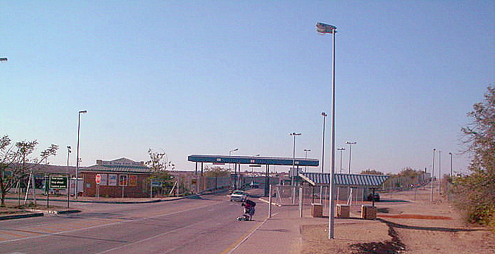 A dusty border crossing between two African countries, with vehicles and pedestrians queued in the hot sun.