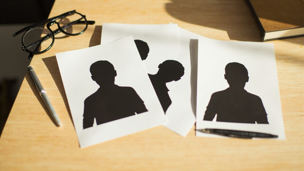 Several printed passport-style photographs fanned out on a desk, each showing a head-and-shoulders silhouette against a plain white backgrou