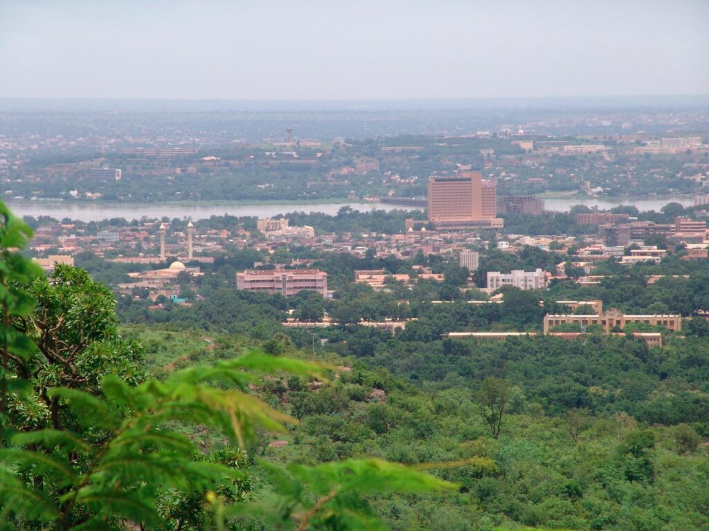 A street scene in Bamako, Mali, with low-rise buildings and pedestrians under bright sunlight, depicting daily life in the West African capi