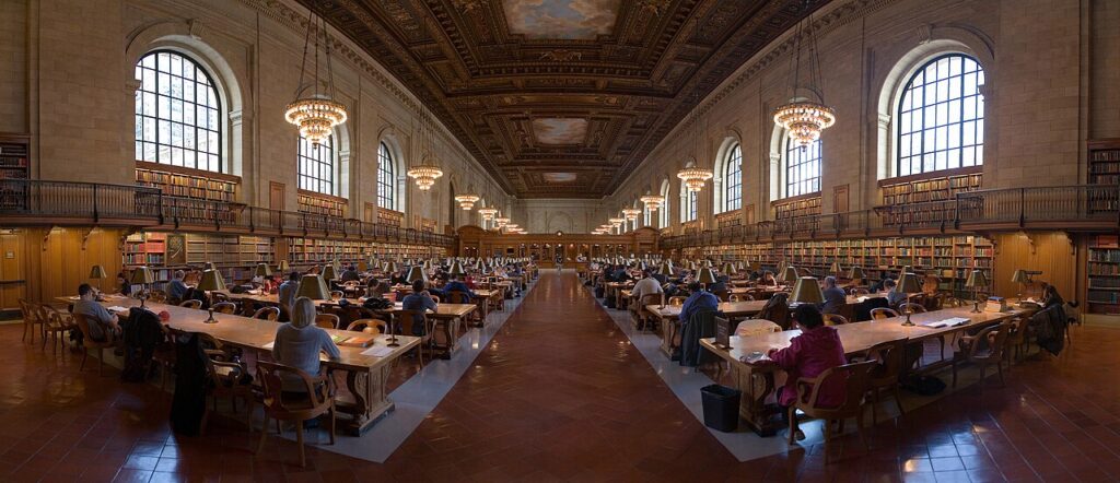 A quiet library reading room with tall wooden bookshelves, long study tables, and soft daylight filtering through arched windows.