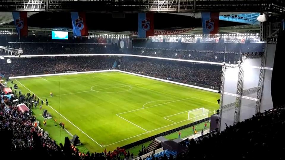 An exterior view of a large football stadium in a coastal Turkish city, photographed in late afternoon light, with the main stand's curved r