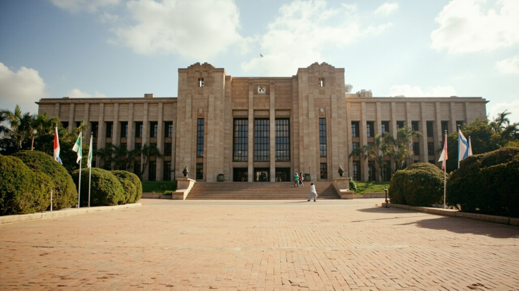 An exterior view of a government administrative building in an African capital, with a paved forecourt, steps and security features visible.