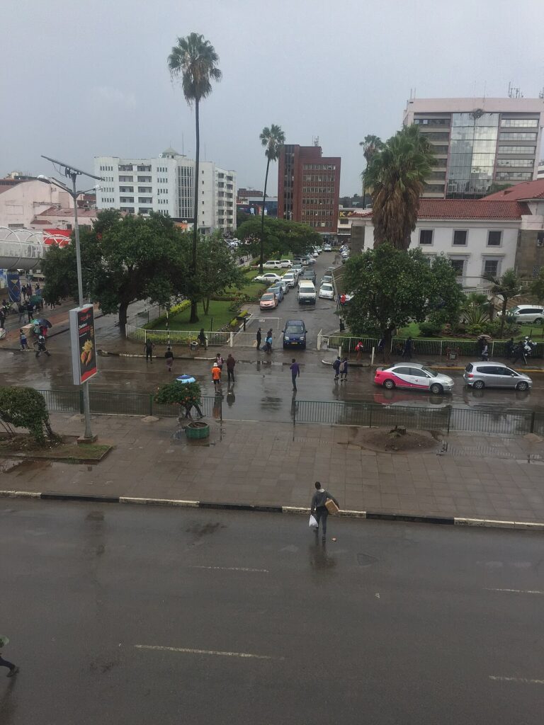 A wide street in an African capital city at dusk with a line of anti-riot police officers in helmets standing at mid-distance.