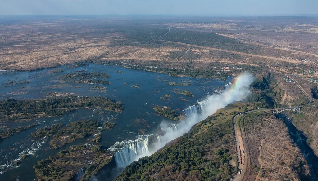 A wide daytime view of Victoria Falls with mist rising from the gorge and green vegetation along the riverbanks.