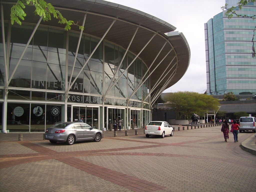 An exterior view of a large modern conference centre with security barriers and uniformed personnel at the entrance during a diplomatic even