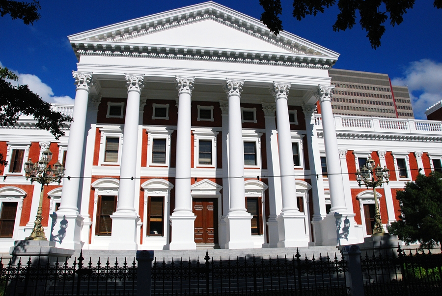 A photograph of the South African Parliament complex in Cape Town, showing the legislative buildings framed by trees.